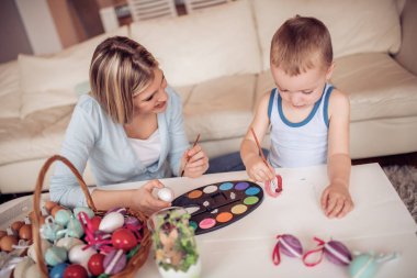 Genç anne oğluyla Paskalya yumurtaları oturma odasında boyama
