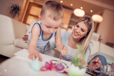 Genç anne oğluyla Paskalya yumurtaları oturma odasında boyama