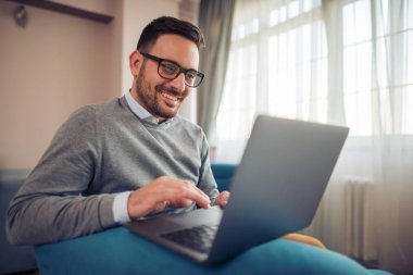 genç adam izliyor ve dizüstü bilgisayarınızda evde çalışma gülümseyen