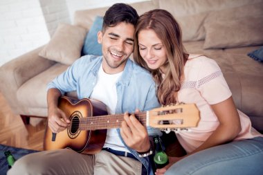 Genç adam şarkı söyleyen kız arkadaşıyla gitar evde oturma odasında