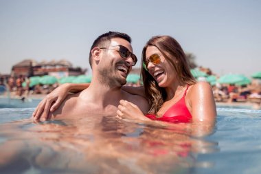 Genç çift sarılma ve yüzme havuzunda gülüyor