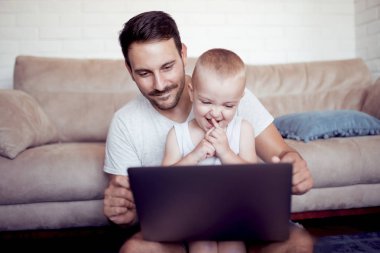 Baba ve oğul evde kanepede dizüstü bilgisayar kullanarak