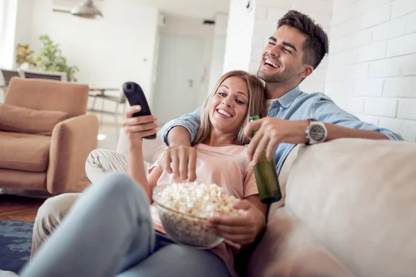 若いカップルがソファの上に横たわって 映画を見て ビールとポップコーンを食べて — ストック写真