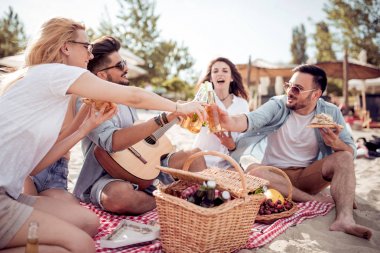 Pizza yeme ve sahilde otururken soğuk bira içme beş genç neşeli insanlar.