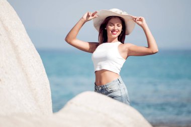 Yaz şapka kaya tarafından deniz plaj kenarında oturan kadın. 