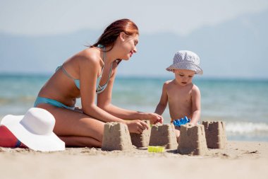 Anne ve oğlu tropik sahilde Kumdan kale yapma.