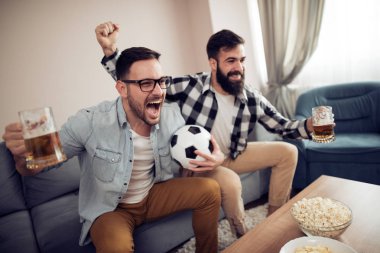 Evde eğlenmek, futbol maçı izlerken mutlu genç arkadaşlar.