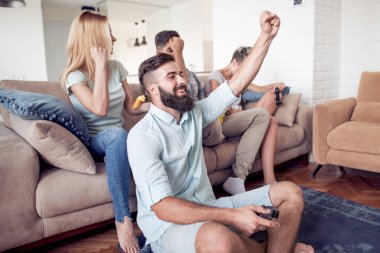 Modern apartmanda oturuyor ve video oyunları oynarken yetişkin arkadaş grubu.