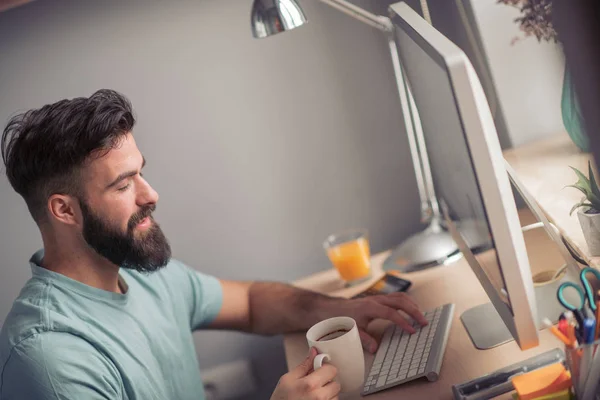 Aantrekkelijk Bebaarde Man Zittend Aan Tafel Werken Computer Drinken Koffie — Stockfoto