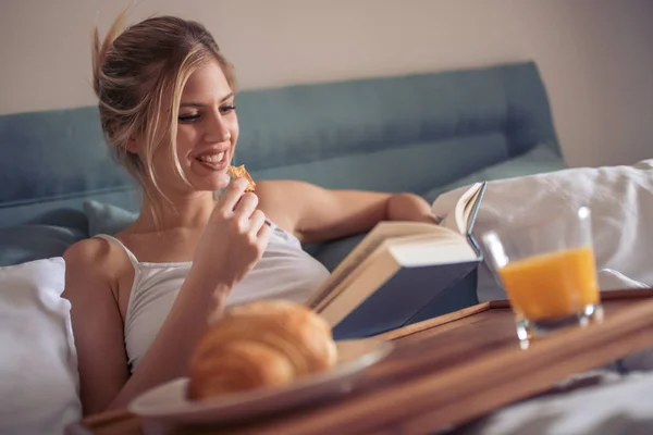 Ευτυχισμένη Γυναίκα Διαβάζοντας Βιβλίο Και Φαγητό Στο Κρεβάτι Πρωί — Φωτογραφία Αρχείου