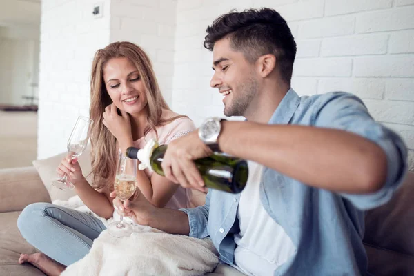 Loving young couple with wine glasses sitting in living room at home.