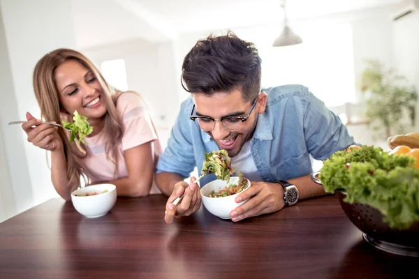 Portrait of young loving couple eating healthy salad for lunch in kitchen.