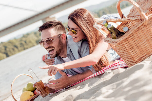 Portrait of happy couple laying on the beach with fruit basket.
