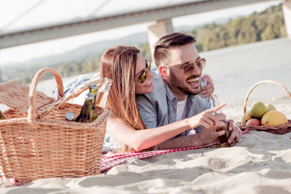 Portrait of happy couple laying on the beach with fruit basket.