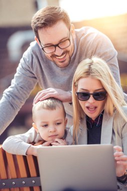 Mutlu genç aile açık havada dizüstü bilgisayar ile eğleniyor.
