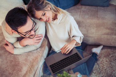 Genç çift oturma odası ve dizüstü bilgisayar kullanarak oturuyorlar.