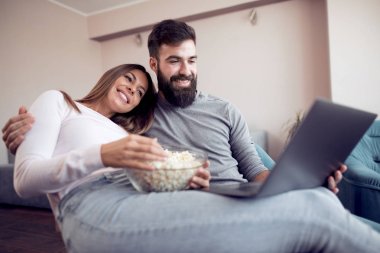 Evde patlamış mısır ile kanepede oturan ve dizüstü film izlerken mutlu genç Çift.