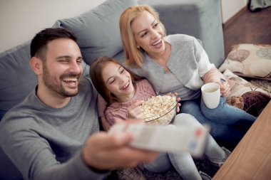 Baba, anne ve kızı Tv izlerken ve evde oturma odasında patlamış mısır yemek.