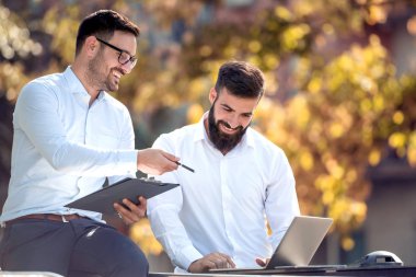 İki yakışıklı işadamları bir dizüstü bilgisayar kullanarak ve açık ayakta iken gülümseyen.