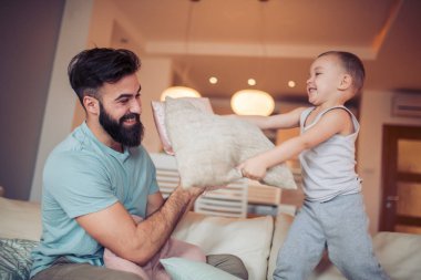 Küçük bir çocuk ve babası yastık ile mücadele ve yatağa evde otururken gülümseyen.