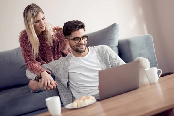 放松爱的年轻夫妇与咖啡使用笔记本电脑在家里的沙发上 — 图库照片