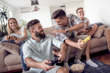 Modern apartmanda oturuyor ve video oyunları oynarken yetişkin arkadaş grubu.