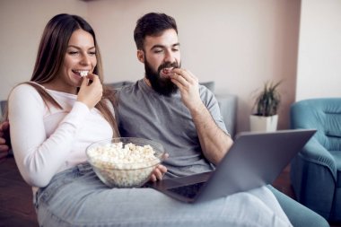 Evde patlamış mısır ile kanepede oturan ve dizüstü film izlerken mutlu genç Çift.