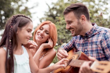 Mutlu aile kavramı-baba gitar çalıyor, anne ve kızı bir şarkı söyle.