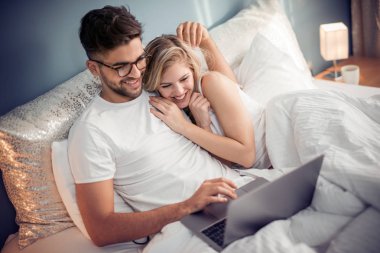 Mutlu çift yatak üstünde laptop ile. Erkek ve kadın yatak odasında dinlenirken dizüstü video izlerken zevk.