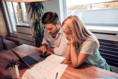 Genç çift mali, dizüstü bilgisayar ve hesap makinesi kullanarak yönetme. Kadın ve evrak birlikte, ödeme vergi online yapan erkek.