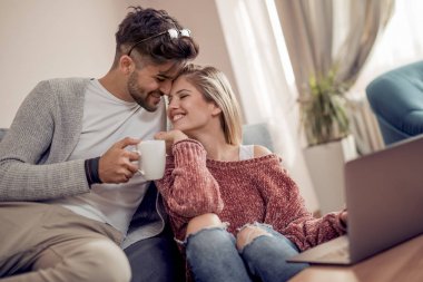 kanepede oturan ve evde dizüstü bilgisayar kullanarak bir çift.