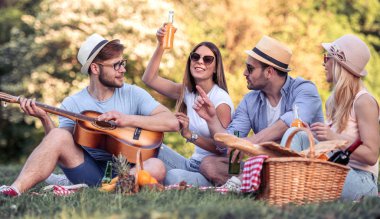Mutlu genç arkadaşlarım parkta piknik. Onlar tüm mutlu, eğleniyor, gülümseyen ve gitar çalmak vardır.