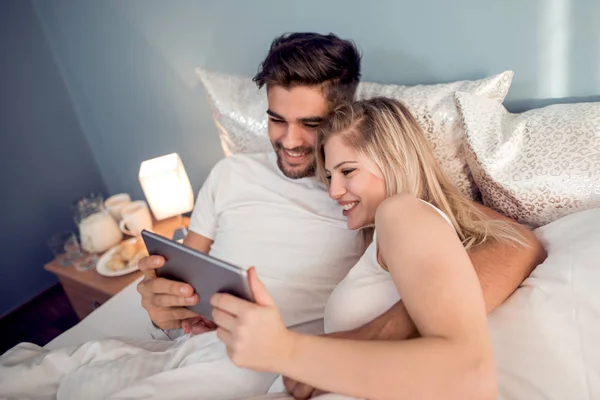 幸福的年轻夫妇躺在床上使用片剂 — 图库照片