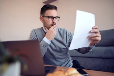 Kanepede oturan ve evde dizüstü bilgisayarda çalışma gözlük içinde genç serbest meslek 