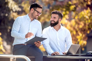 Dizüstü bilgisayar kullanarak ve açık havada konuşurken iki iş adamları
