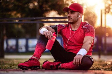 Atletik adam dışarıda otururken şişeden su içiyor..