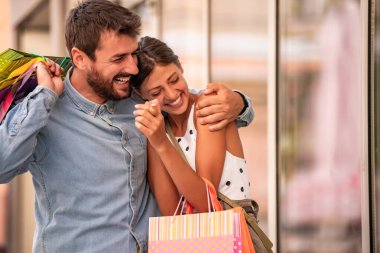 Alışveriş yaptıktan sonra gülümseyen ve kocaman çantalı mutlu bir çiftin portresi.