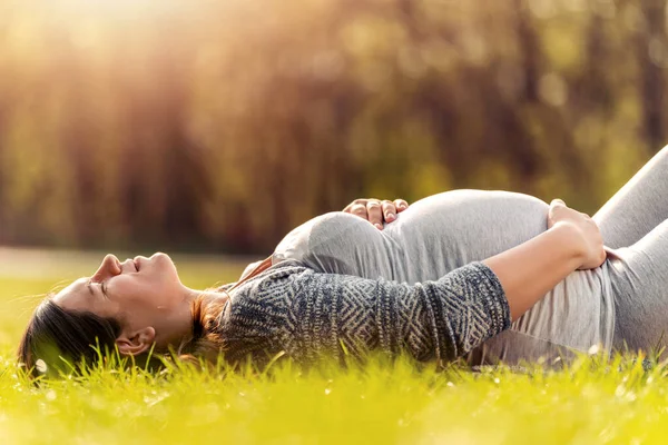 美丽的孕妇躺在草地上 在阳光灿烂的日子 — 图库照片
