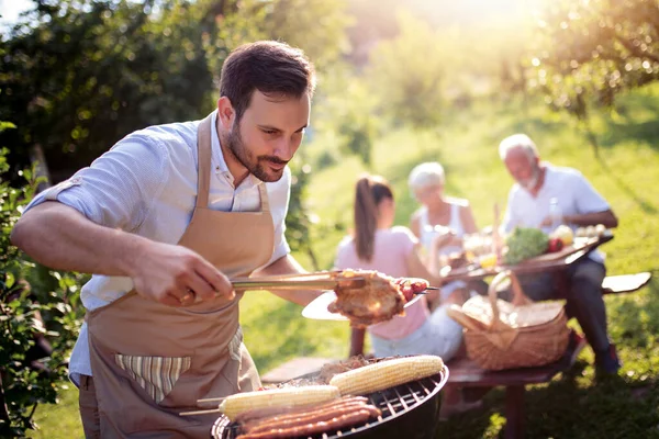 トウモロコシ ソーセージ 肉を焼く若い男 家族は庭でバーベキューをしている — ストック写真