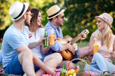 Mutlu bir arkadaş grubu parkta eğleniyor ve gülümsüyor. Gitar çalıyorlar..