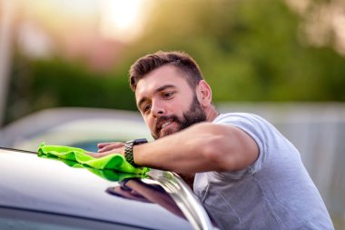 Genç bir adamın portresi, gün ışığında açık havada arabasını bir bezle temizliyor..