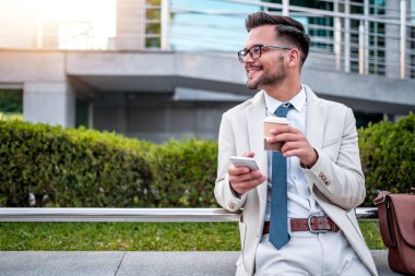 Genç işadamının molası var, kahve içiyor ve dışarıda cep telefonu kullanıyor..