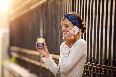 Güneşli bir günde sokakta yürüyen ve akıllı telefon kullanan bir kadın..
