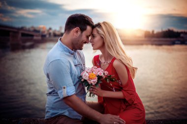 Birbirini seven bir çift gülüyor ve nehir kenarında oturuyor..