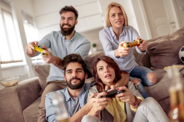 Modern bir dairede oturan ve video oyunları oynayan bir grup genç arkadaş. Arkadaşlık, teknoloji, oyunlar ve ev kavramı.