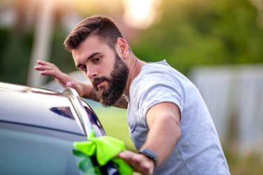 Arabasını dışarıda bir bezle temizleyen genç bir adamın portresi..