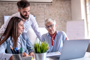 İş arkadaşları onu ofis masasında dinlerken genç adam gülümseyerek bir şey tartışıyor..