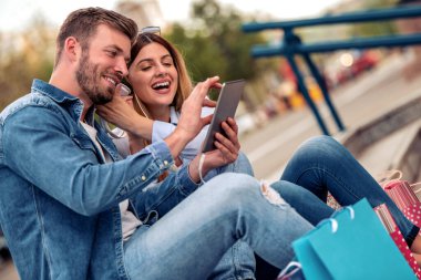 Alışveriş çantalı mutlu çift akıllı telefonlu müzik dinliyor..