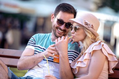 Bankta oturup meyve suyu içen gülümseyen çiftin portresi..