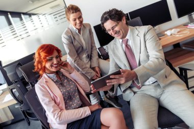 İş adamları ofiste çalışırken tablet kullanıyor ve gülümsüyorlar..